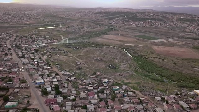 A township in South Africa with small low cost housing and informal shanty shack structures as a vehicle drives along the road.