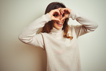 Young beautiful woman wearing winter sweater standing over white isolated background Doing heart shape with hand and fingers smiling looking through sign
