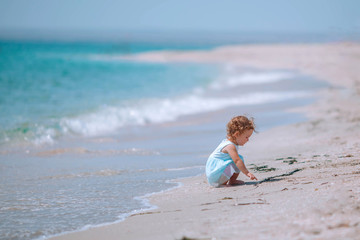 A pretty girl sits on the sand by the sea.
