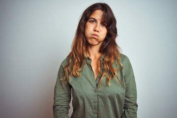 Fototapeta premium Young beautiful woman wearing green shirt standing over grey isolated background puffing cheeks with funny face. Mouth inflated with air, crazy expression.