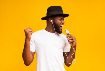 Happy african man in hat singing into smartphone like microphone - Powered by Adobe