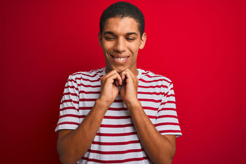 Young handsome arab man wearing striped t-shirt over isolated red background laughing nervous and...