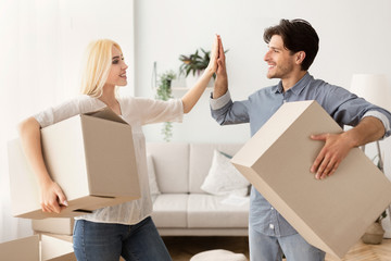 Husband And Wife Giving High-Five Carrying Moving Boxes In House