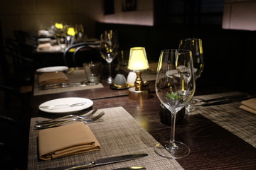 close up wine glass, fork, knife and napkin on table of western food restaurant at night. Defocused background