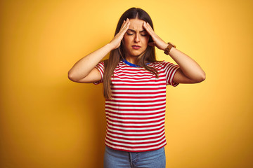 Young beautiful woman wearing striped t-shirt standing over isolated yellow background with hand on head for pain in head because stress. Suffering migraine.
