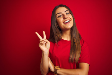 Young beautiful woman wearing t-shirt standing over isolated red background smiling with happy face...
