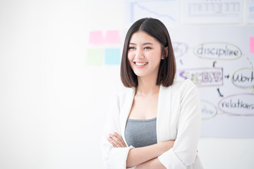 Portrait of young beautiful and confident business woman smiling and standing in front of meeting board or planning chart give the positive attitude of work in the white meeting room as a background.