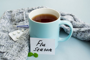 Cold and flu season. Cup with hot tea, mint, thermometer and tablets on a light background. Treatment and prevention of the virus. - obrazy, fototapety, plakaty
