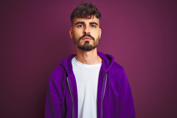 Obraz premium Young man with tattoo wearing striped polo standing over isolated yellow background with serious expression on face. Simple and natural looking at the camera.