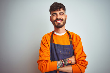 Young shopkeeper man with tattoo wearing apron standing over isolated white background happy face...