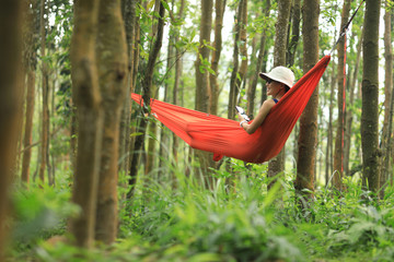 Obraz na płótnie Canvas Woman relaxing in hammock with smartphone in tropical rainforest