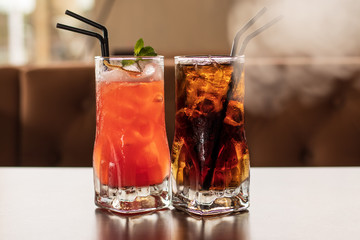 Two glasses of cocktails with ice and straws on the table. Fresh cold drink with lemon. Bright orange cocktail. Yellow transparent liquid. Frozen.