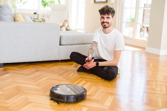 Young man using automatic vacuum cleaner to clean the floor, controling machine housework robot