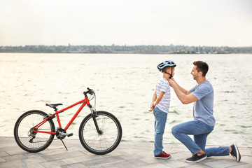 Fototapeta premium Father helping his son to put on helmet before riding bicycle outdoors