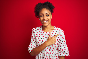 African american woman wearing fashion white dress standing over isolated red background cheerful with a smile of face pointing with hand and finger up to the side with happy and natural expression 