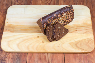 Partly sliced brown bread triangular shape on wooden cutting board