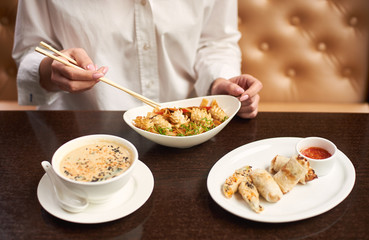 Woman in white blouse sitting in luxury restaurant and eating tasty meal. Three courses lunch from soup, noodles and tempura shrimps on special offer. Girl with manicure tasting oriental style dish.