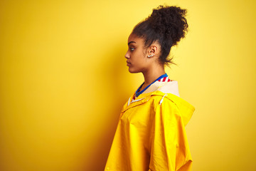 Obraz na płótnie Canvas Young african american woman wearing rain coat over isolated yellow background looking to side, relax profile pose with natural face with confident smile.