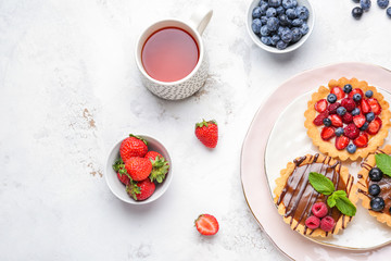 Sweet tartlets with berries and tea on light table