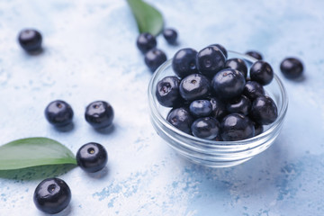 Bowl with fresh acai berries on color background