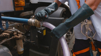man with safety equipment connecting water hose valve on water truck