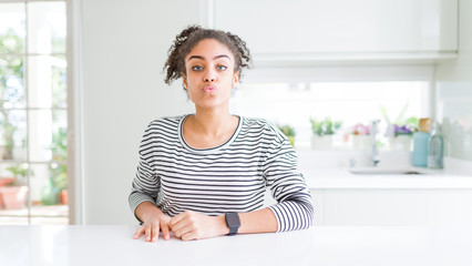 Beautiful african american woman with afro hair wearing casual striped sweater looking at the camera blowing a kiss on air being lovely and sexy. Love expression.