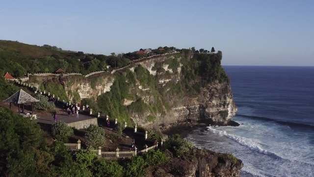 Flying backwards, aerial view of observation deck with tourists, high coastline and wonderful ocean. Bali, Indonesia