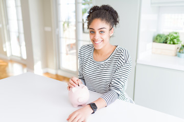 Young african american woman putting a coin inside piggy bank as invest or saving with a happy face...