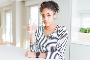 Young african american girl drinking a fresh glass of water with a confident expression on smart face thinking serious
