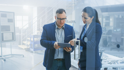 Female and Male Engineer Work in a High Tech Development Facility Holding a Tablet Computer. They...