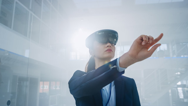 Female Engineer Using Augmented Reality Headset Pushes Virtual Buttons in the Air. In Innovation High Tech Laboratory Facility with Futuristic Atmosphere.
