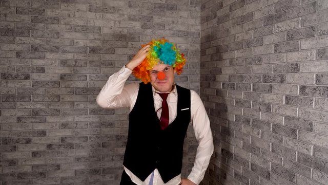 A man picks his nose at work. Office worker in clown wig, clown concept at work. Businessman with clown wig. Original clown costume for Halloween