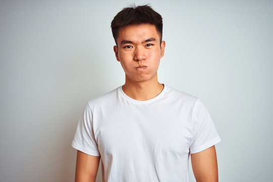 Young asian chinese man wearing t-shirt standing over isolated white background puffing cheeks with funny face. Mouth inflated with air, crazy expression.