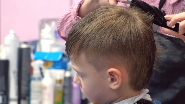 Hairdresser cuts hairs with scissors on boy's head. Side view, stylist's hands close-up