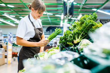 Shop assistant in supermarket re-stocking fresh vegetables