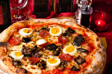 Italian pizza with fried eggplants, hot salami, eggs and green peas