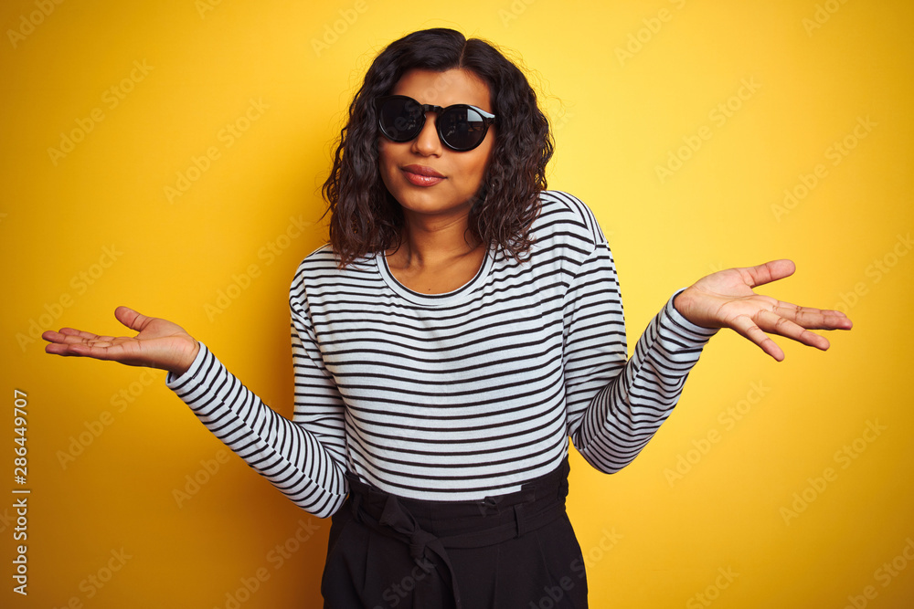 Wall mural Transsexual transgender woman wearing sunglasses over isolated yellow background clueless and confused expression with arms and hands raised. Doubt concept. - Wall murals