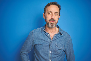 Handsome middle age senior man with grey hair over isolated blue background puffing cheeks with funny face. Mouth inflated with air, crazy expression.