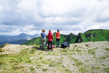 three unrecognizable girls on the edge of mountain looking on the green alps landscape