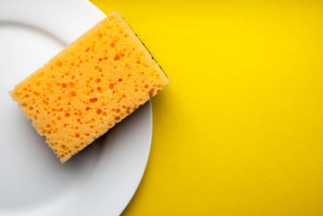 Cleaning sponge on a white plate on a yellow background