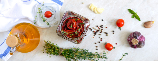 Sun-dried tomatoes with herbs, garlic in olive oil in a glass jar on a light background. Top view, flat lay. Banner