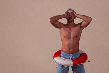 Drei Viertel Länge von einem hemdslosen Mann steht vor braunen Hintergrund. Mit Rettungsring und Duschhaube mit beiden Händen an dem Kopf.