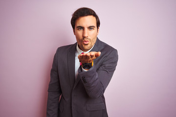 Young handsome businessman wearing suit and tie standing over isolated pink background looking at the camera blowing a kiss with hand on air being lovely and sexy. Love expression.