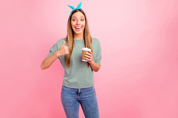 Pretty lady holding hot beverage raising thumb up wear striped pullover isolated pink background