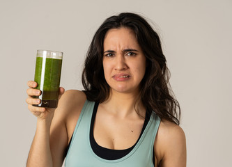 Beautiful young sports latin woman boring of diet holding green smoothie in dislike