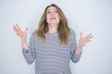 Fototapeta na wymiar Beautiful blonde girl with blue eyes wearing striped sweater over white isolated background crazy and mad shouting and yelling with aggressive expression and arms raised. Frustration concept.
