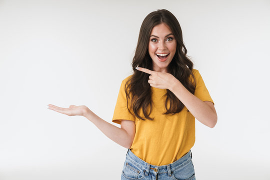 Image of amazed brunette woman wearing casual clothes smiling and pointing fingers at copyspace on her palm
