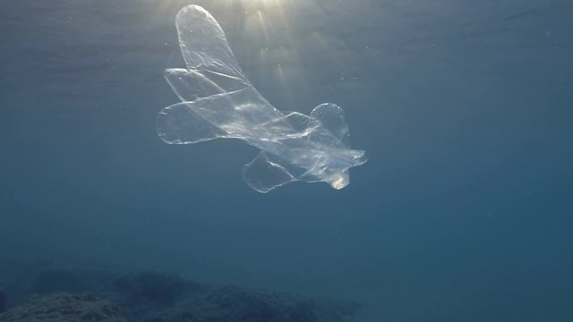  Plastic pollution, Discarded plastic glove slowly drifting under surface of blue water in the sunset light. Transparent plastic glove floats in Mediterranean Sea, Europe. Slow motion