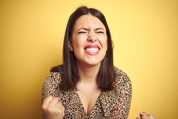 Young beautiful brunette woman wearing leopard shirt over yellow isolated background very happy and excited doing winner gesture with arms raised, smiling and screaming for success.