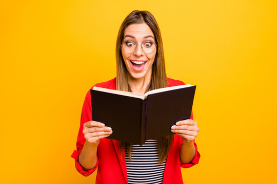 Portrait of astonished hipster with long hair holding printed fiction book wearing eyeglasses eyewear isolated over yellow background